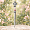 Silver-toned Sweet Elephant pen with grey and pink beads in a soft botanical garden setting